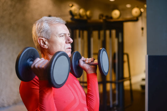 Older man lifting dumbbells at a gym, illustrating strength training across the lifespan