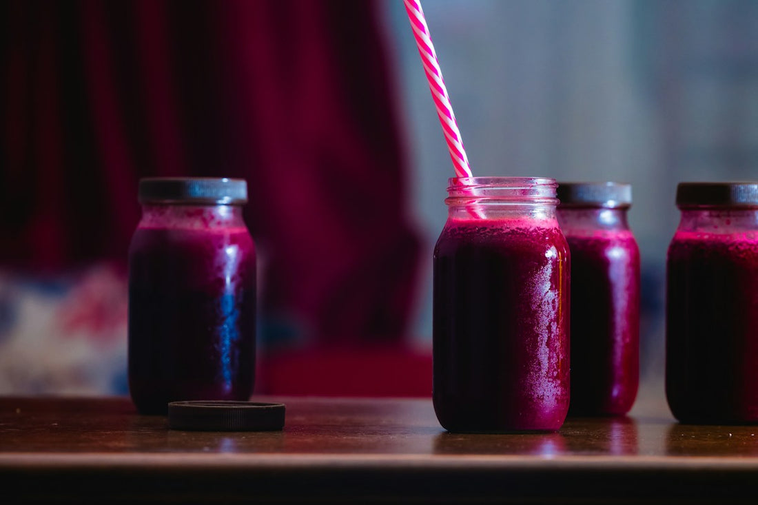 Two jars of red juice on a table with a rustic food backdrop