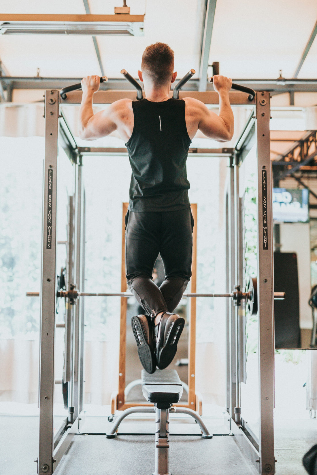 Man in a black sleeveless top performing a pull-up on an indoor gym bar