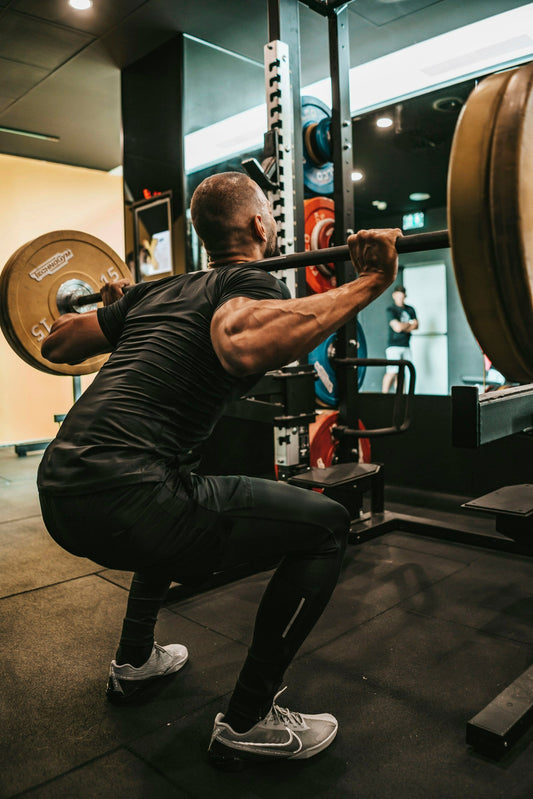 Muscular athlete under a barbell performing a controlled squat in a gym