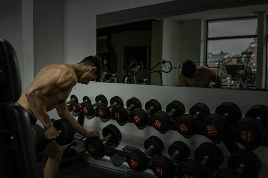 Muscular lifter training with dumbbells in a gym mirror
