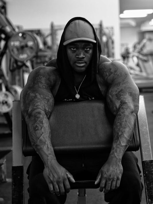 A focused lifter in a dark gym hoodie sitting beside strength equipment, illustrating quiet-work pump-cover style