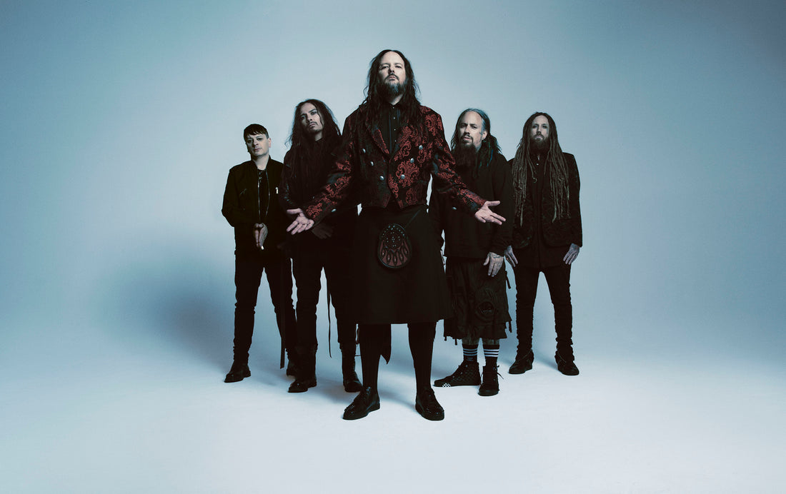 Korn band members in a studio group portrait with Jonathan Davis at center against a pale backdrop.