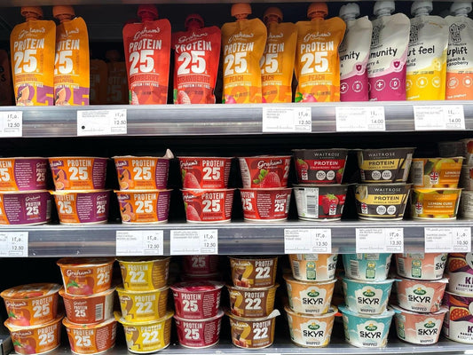 Supermarket refrigerated shelf stocked with high-protein yogurt tubs and drinks in multiple flavors