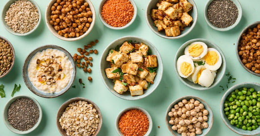 Overhead arrangement of bowls containing tofu, hard-boiled eggs, lentils, chickpeas, peas and seeds