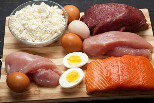 Assortment of chicken salmon eggs cottage cheese and other protein-rich foods on a wooden board