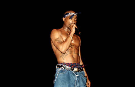 Tupac Shakur performing shirtless with a blue bandana, showing a lean chest and arms