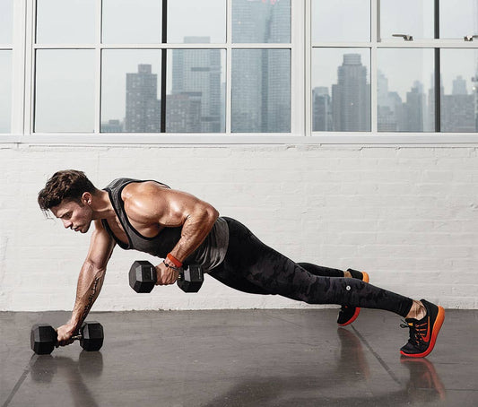 Man performing a renegade dumbbell row in a high plank in a bright gym