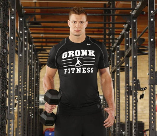 Rob Gronkowski in a black Gronk Fitness shirt holding a dumbbell inside a gym