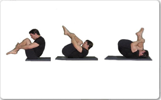 A man practicing the rolling-like-a-ball Pilates movement on a blue exercise mat with knees hugged to the chest.