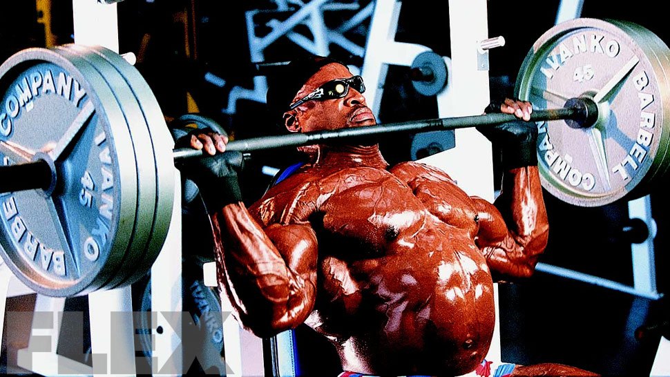 Ronnie Coleman pressing a heavily loaded barbell while seated on a gym bench