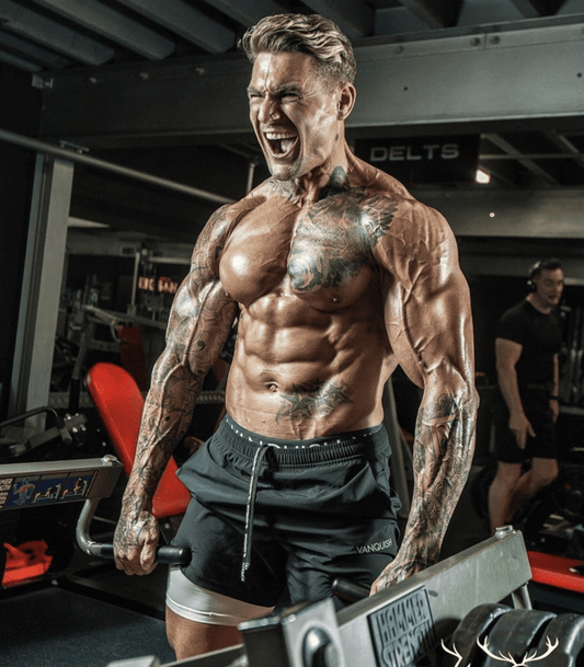 Ross Dickerson seated in a gym showing muscular chest, arms and defined abs