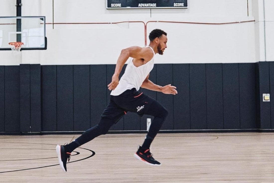 Stephen Curry sprinting on an indoor basketball practice court wearing a white sleeveless training top