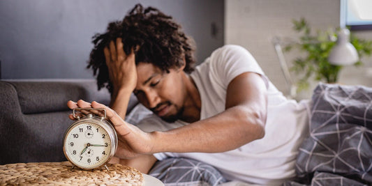 A tired man waking beside an alarm clock after too little sleep