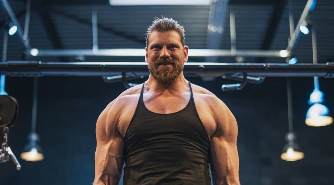 Olivier Richters, the Dutch Giant, standing in a gym wearing a black tank top with developed shoulders and arms