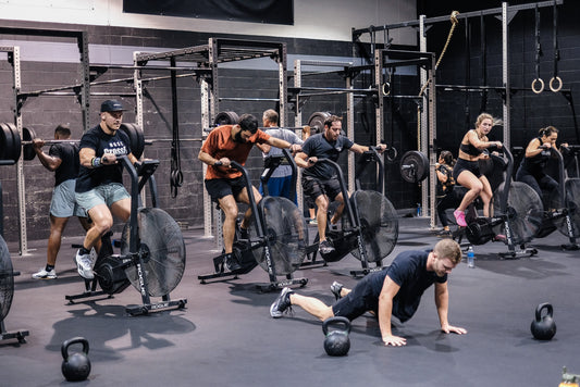 CrossFit gym group riding air bikes while another athlete works on the floor beside kettlebells