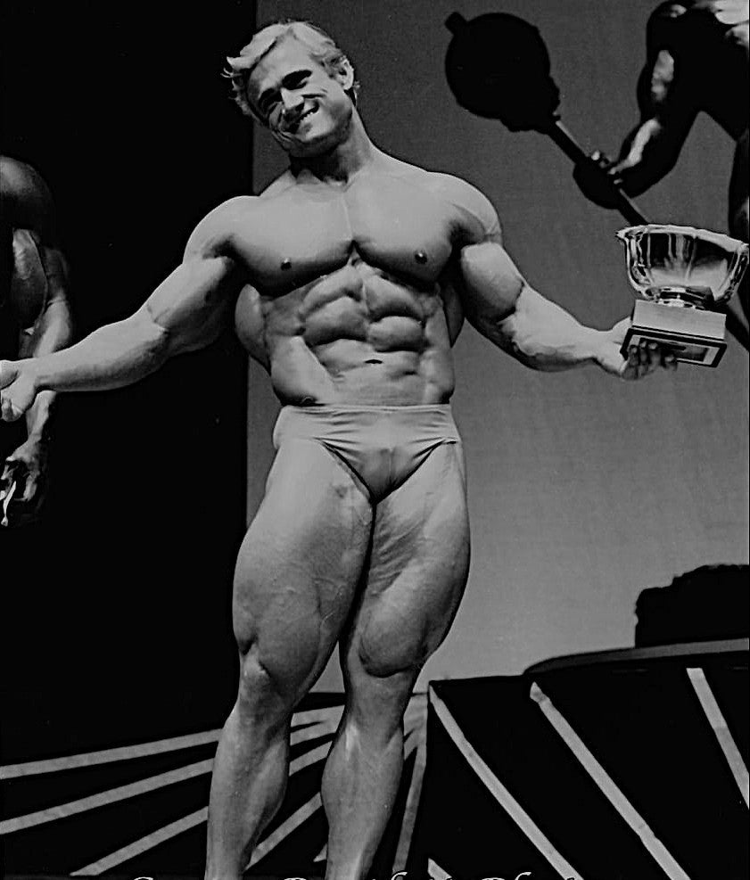 Tom Platz posing with exceptionally developed legs while holding a trophy at the 1981 Mr. Olympia