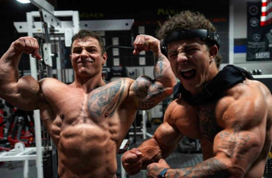 Christian and Michael Gaiera, the Tren Twins, posing together in a gym wearing sleeveless training tops