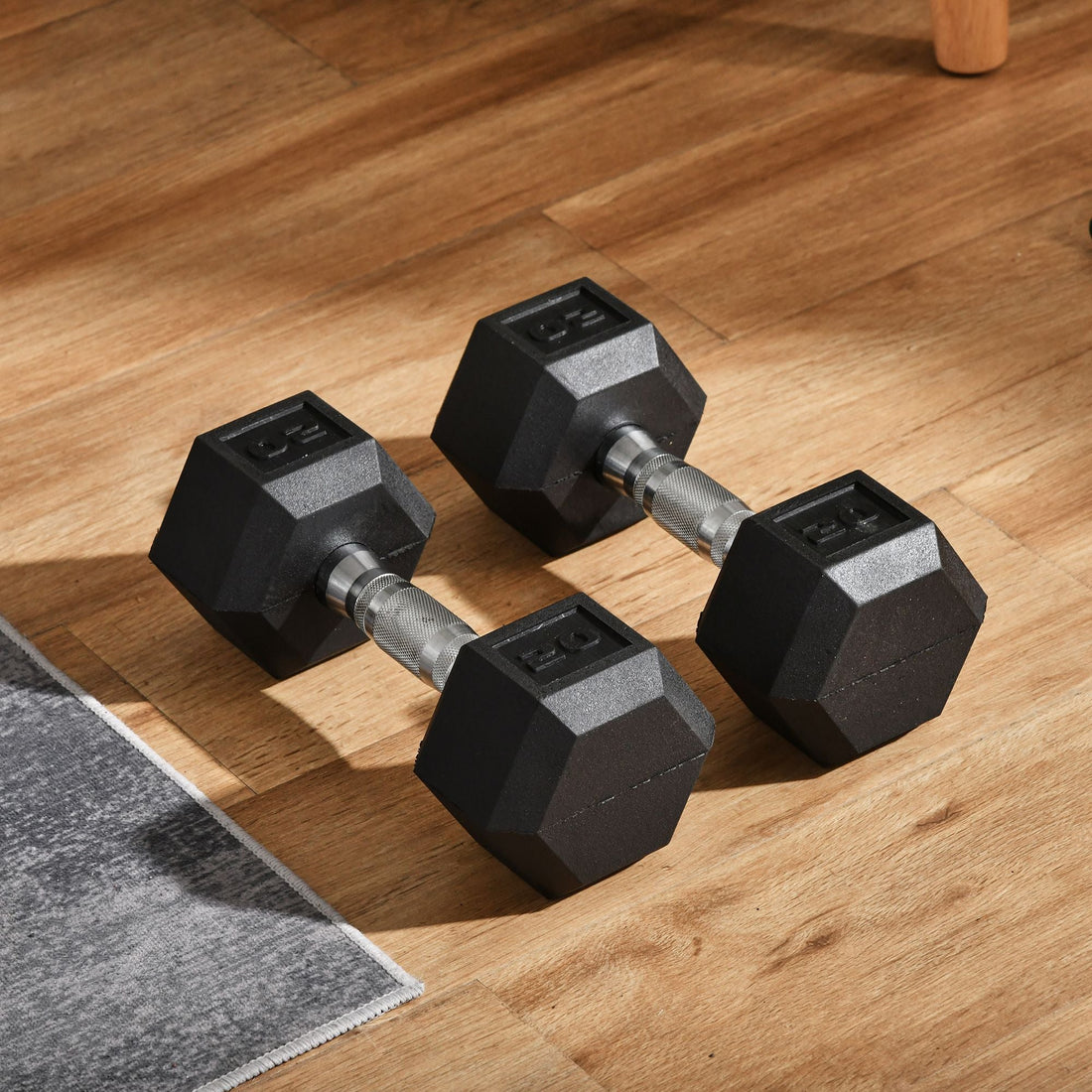Two black hexagonal dumbbells on a wooden floor beside a workout mat
