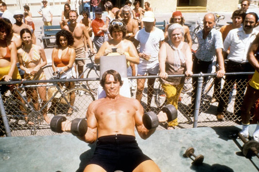 Arnold Schwarzenegger performing seated dumbbell curls during the Golden Era of bodybuilding