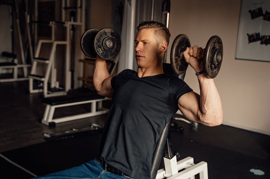 Lifter performing a dumbbell shoulder press in a gym