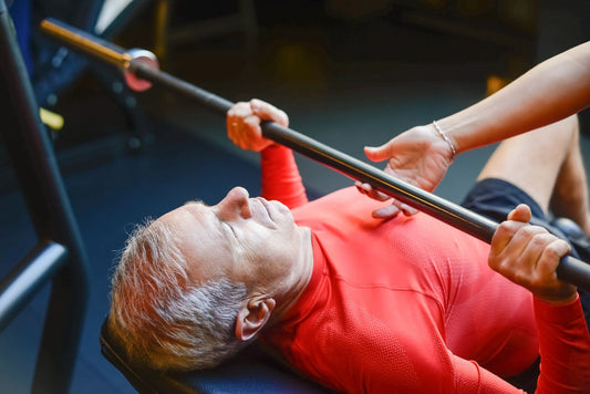 Older male lifter bench pressing with assistance in a gym
