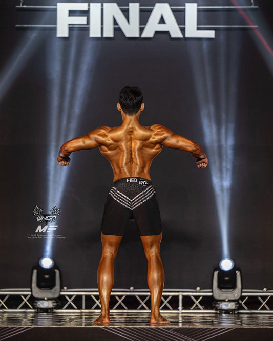 Men's Physique competitor posing under competition lights