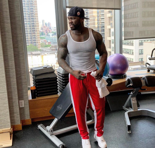 50 Cent resting in a gym in a white tank top, showing muscular arms and shoulders