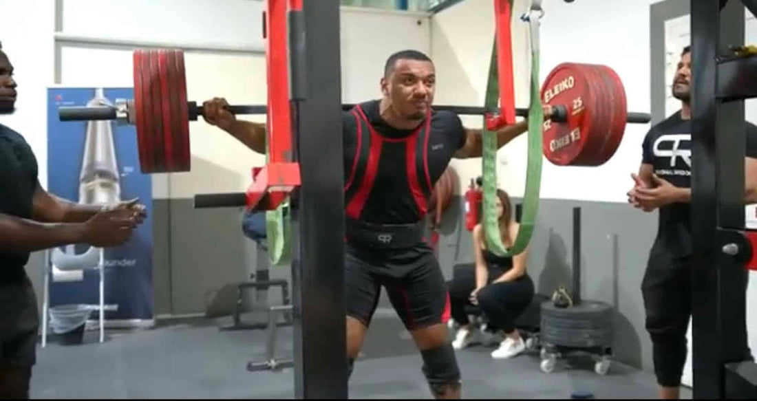 Larry Wheels squatting a heavily loaded barbell in a powerlifting gym with a spotter