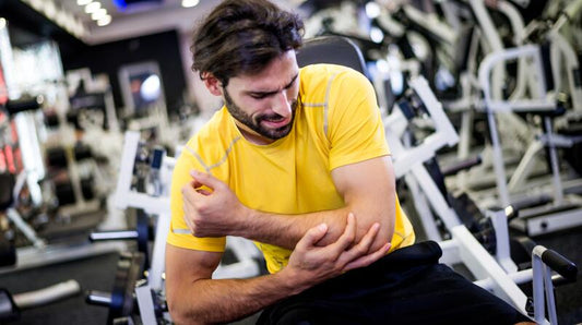 A male gym-goer in a yellow training shirt holding his painful elbow while seated among weight machines
