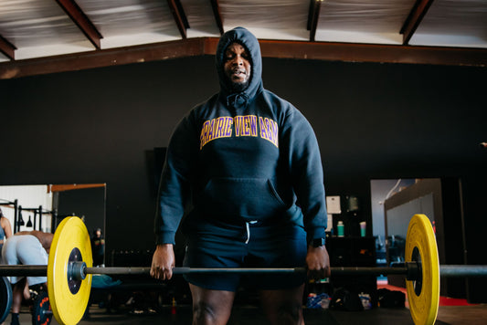 Athlete wearing a dark hoodie holding a barbell in a gym