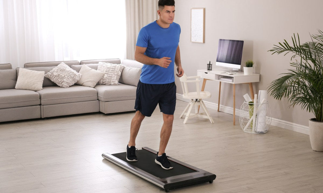 Man walking on a compact treadmill in a bright home living room beside a sofa and desk