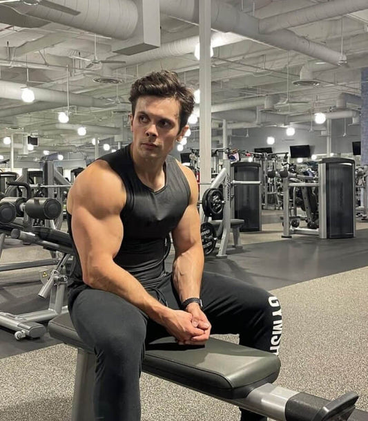 Will Tennyson seated in a black sleeveless gym shirt on a workout bench, showing muscular arms in a weight room