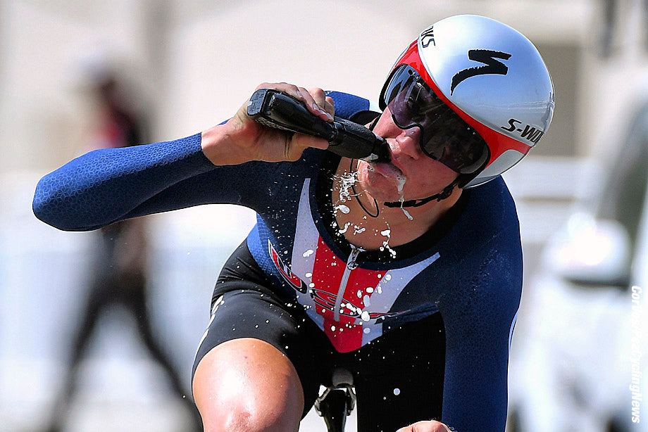 Cyclist in a time-trial helmet rinsing and expelling liquid from a sports bottle during a race