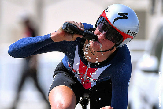 Cyclist in a time-trial helmet rinsing and expelling liquid from a sports bottle during a race