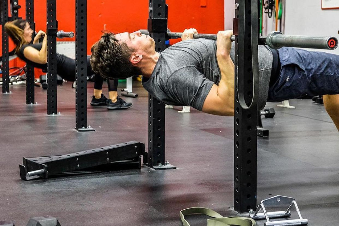 Man in gray shirt pulling his chest toward a fixed bar inside a red-and-black gym
