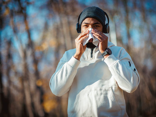 Runner in athletic clothing blowing his nose into a tissue during an outdoor workout