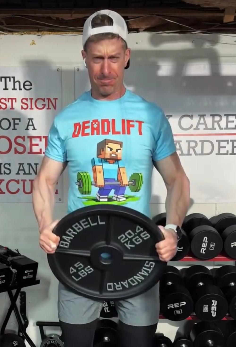 NoFate247 home gym influencer Jonathan holding heavy dumbbells while wearing a funny Deadlift gym t-shirt from Next Cult Brand, featured in the NoFate247 gym merch collection for home gym lifters, arm day fans, and fitness apparel shoppers.